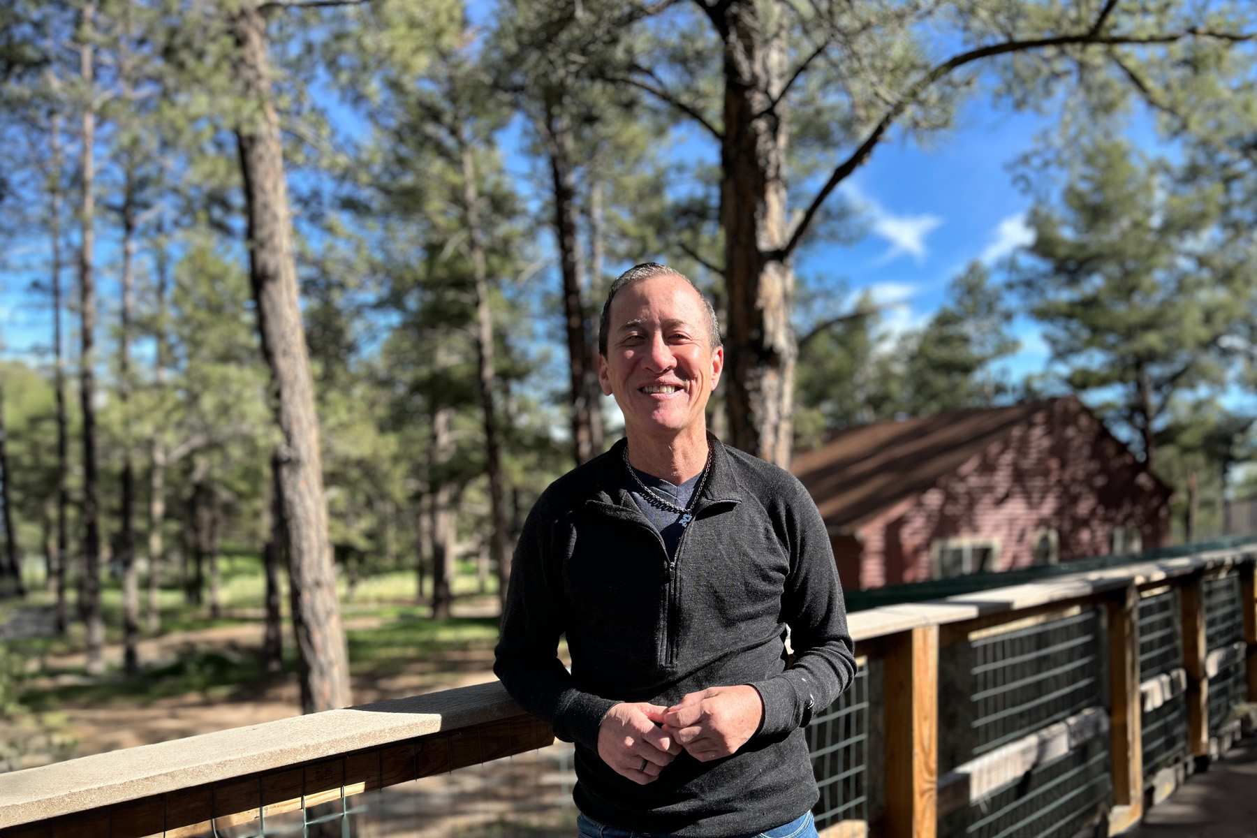 An image of Willy Chang Wilkinson on a deck at Camp Lost Boys. A cabin is in the background to his left.