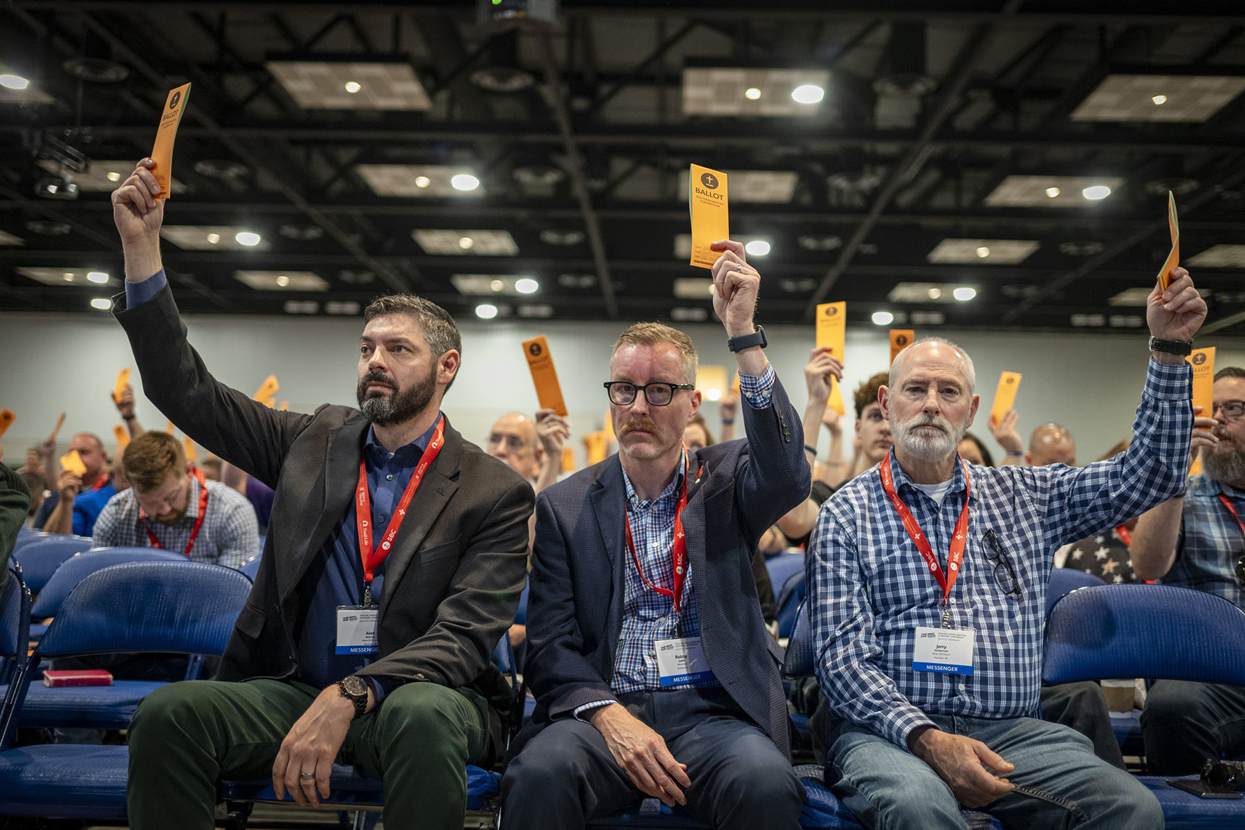 Three men raise their ballots during a Southern Baptist Convention annual meeting.