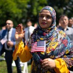 A woman raises her hand as she recites the pledge of allegiance during a naturalization ceremony at George Washington's Mount Vernon.