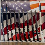 Firearms are seen on display during the National Rifle Association's annual convention. Behind the firearms, a picture of an American flag is displayed.