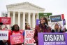 Ruth Glenn addresses a crowd during a rally in front of the Supreme Court as people hold signs behind her.