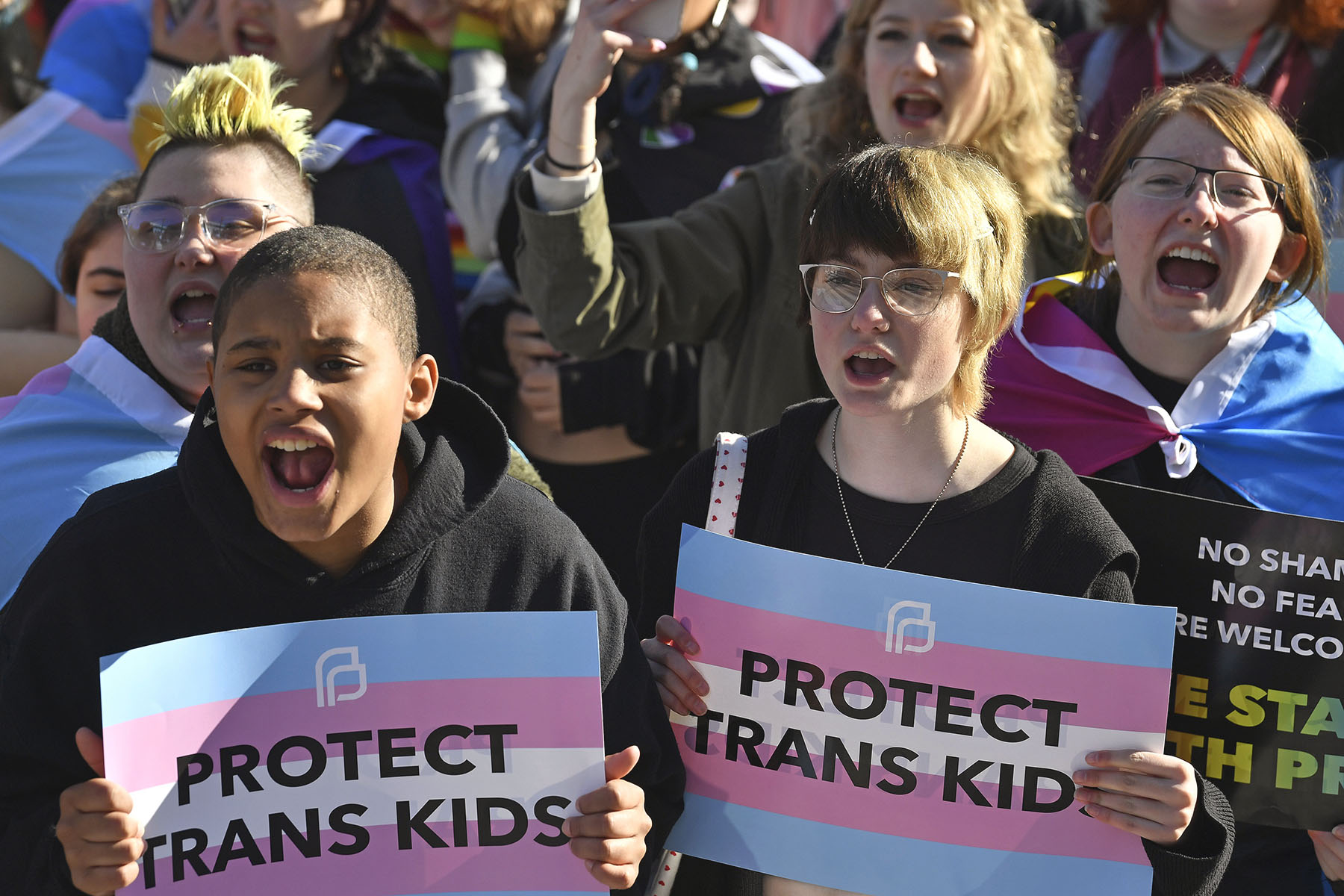 Protesters of Kentucky Senate Bill SB150 cheer on speakers and hold signs up that read "protect trans kids."