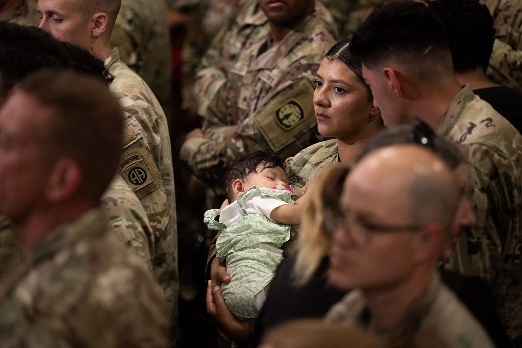 A military woman holds a baby as people wait to hear President Joe Biden address members of the military.