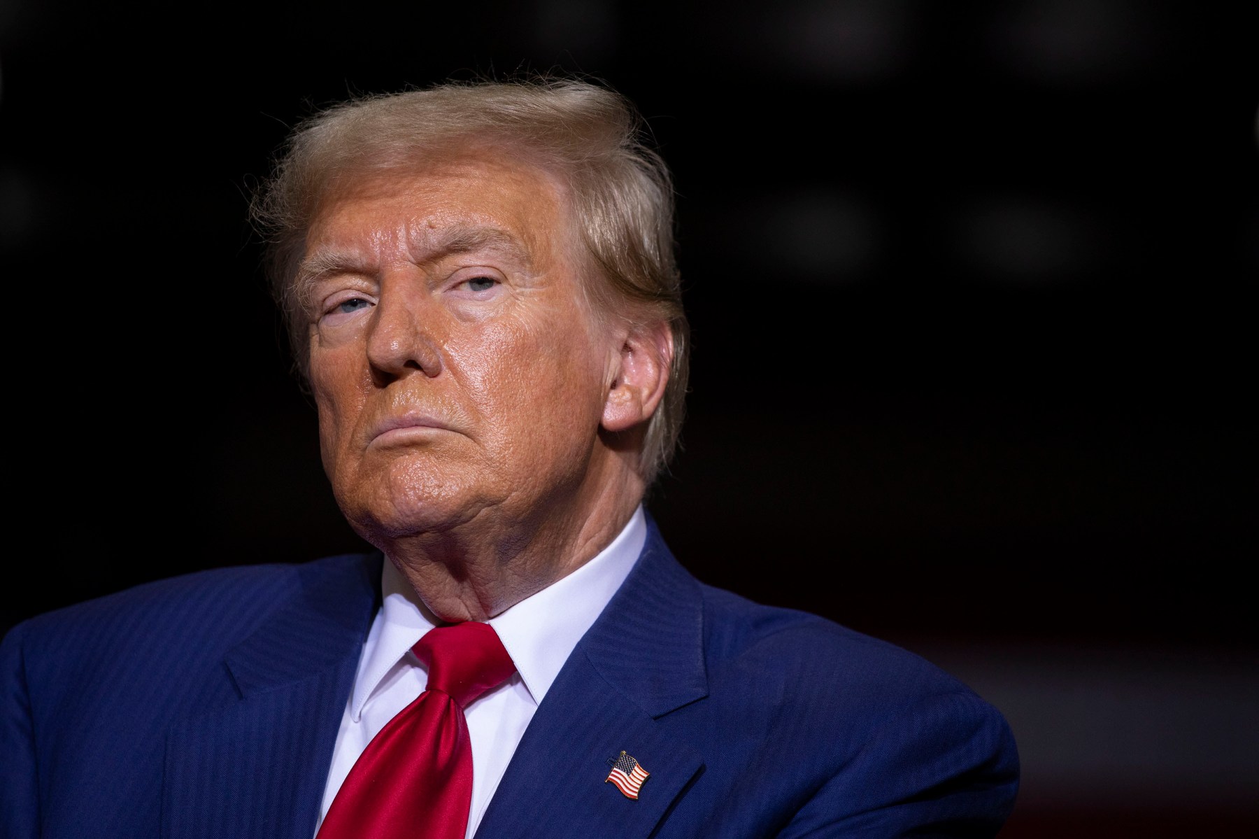 A portrait of Donald Trump, who is wearing a blue suit, red tie and an American flag pin.