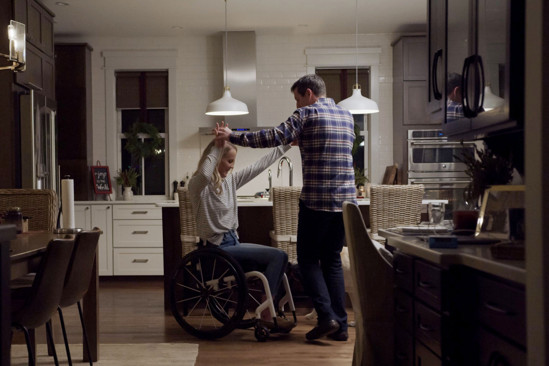 Mallory Weggemann and her husband, Jay Snyder, hold hands as they dance together in a warmly-lit kitchen at night.