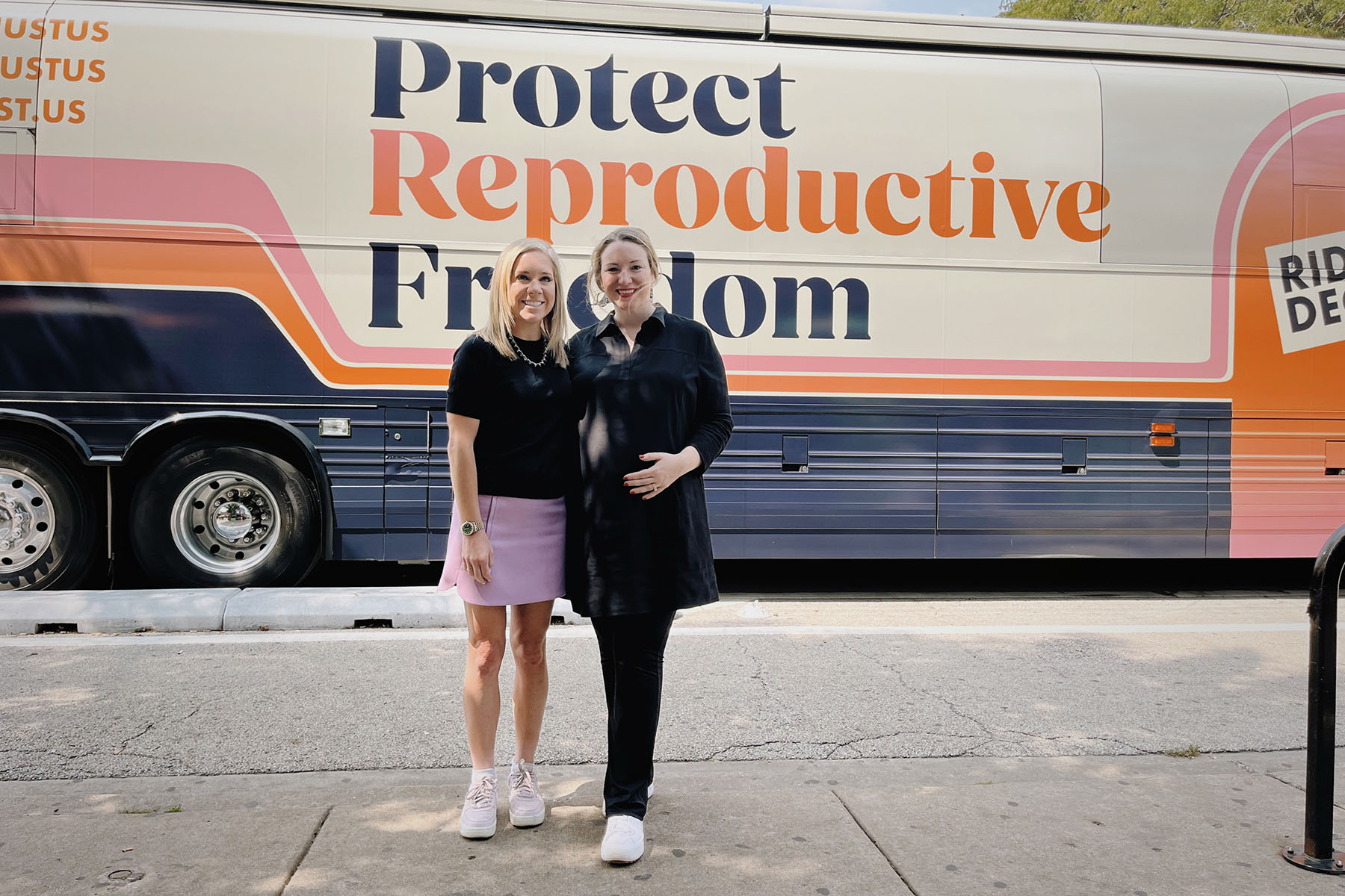 Amanda Zurawski and Kate Cox pose together in front of a bus with a large sign reading "Protect Reproductive Freedom" during a stop on the Fight for Reproductive Freedoms tour.