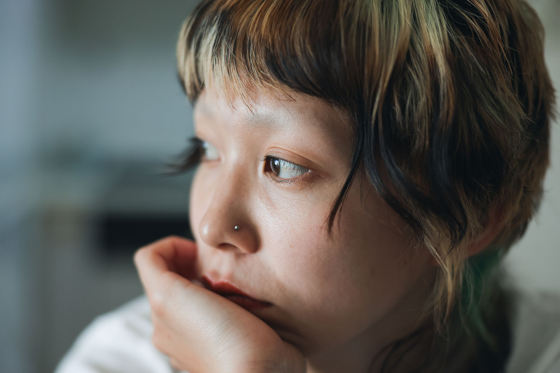 Close up shot of young asian nonbinary person with colorful hair looking away.