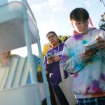 People read banned books outdoors while standing near a book cart.