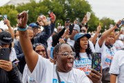 A group of people raising their hands and holding up cell phones during the Crime Survivors Speak March in Washington, D.C. Many are wearing white shirts with slogans like 