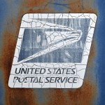 A close-up of a weathered and rusty United States Postal Service (USPS) mailbox. The USPS logo, featuring an eagle, is visibly cracked and peeling on the surface.