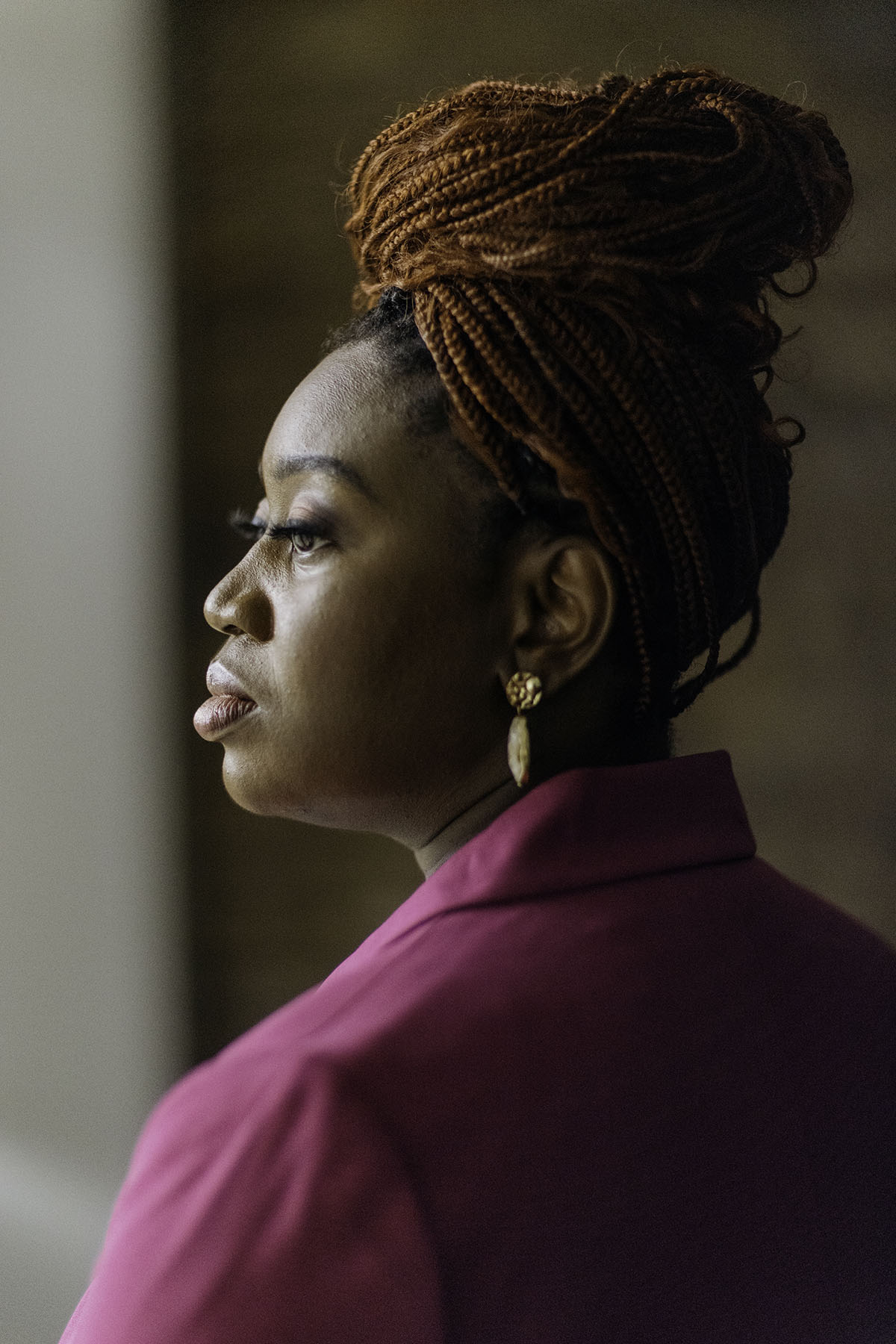 Profile shot of Velvet Scott in a pink suit, looking contemplative. Her braided hair is styled up, and she is wearing gold earrings.