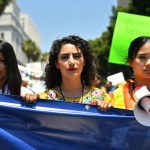 Three protestors carry a large blue banner and a megaphone while participating in a March For Our Lives protest.