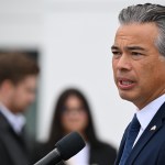 Attorney General Rob Bonta stands at a podium speaking with people in the background.