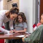 A young girl observes and participates as her guardian shows her the voting process.