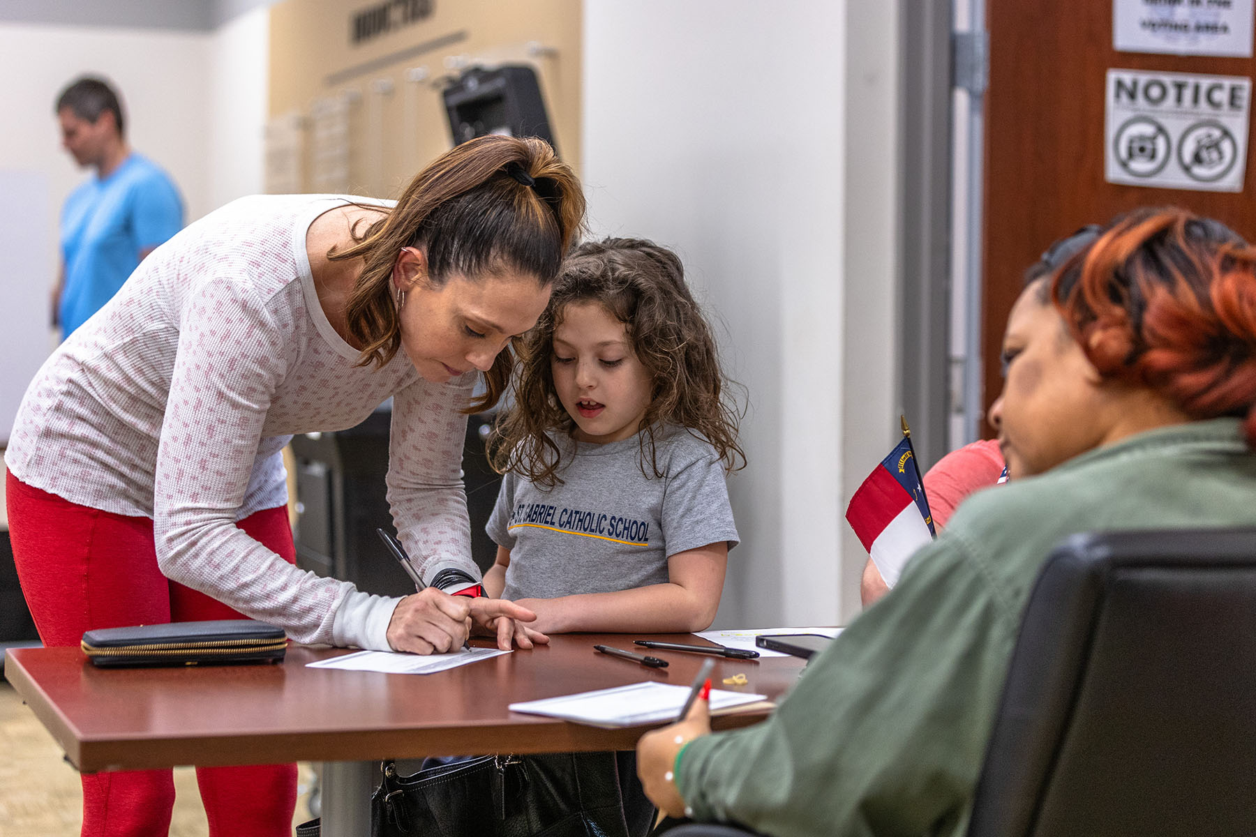 A young girl observes and participates as her guardian shows her the voting process.