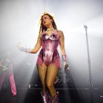 Singer Chappell Roan stands onstage with a microphone in hand and wearing a pink leotard while backlit.