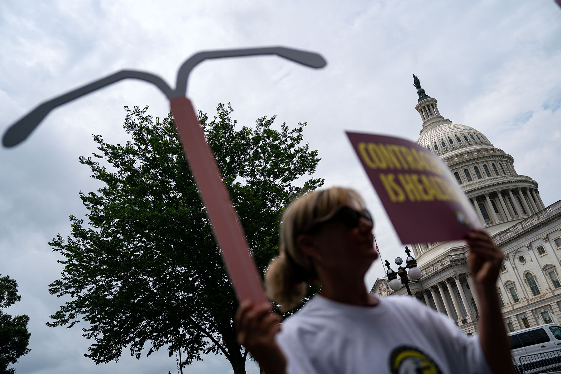 A woman holds up a sign and a replica of a intrauterine device outside the Capitol.