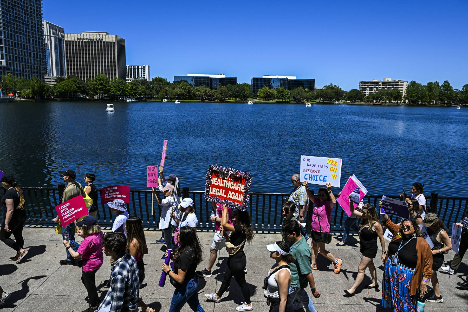 A group of protestors walk with signs past a lake.