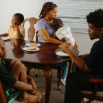 A mother and four of her sons sit at the dinner table, all facing and looking in different directions.