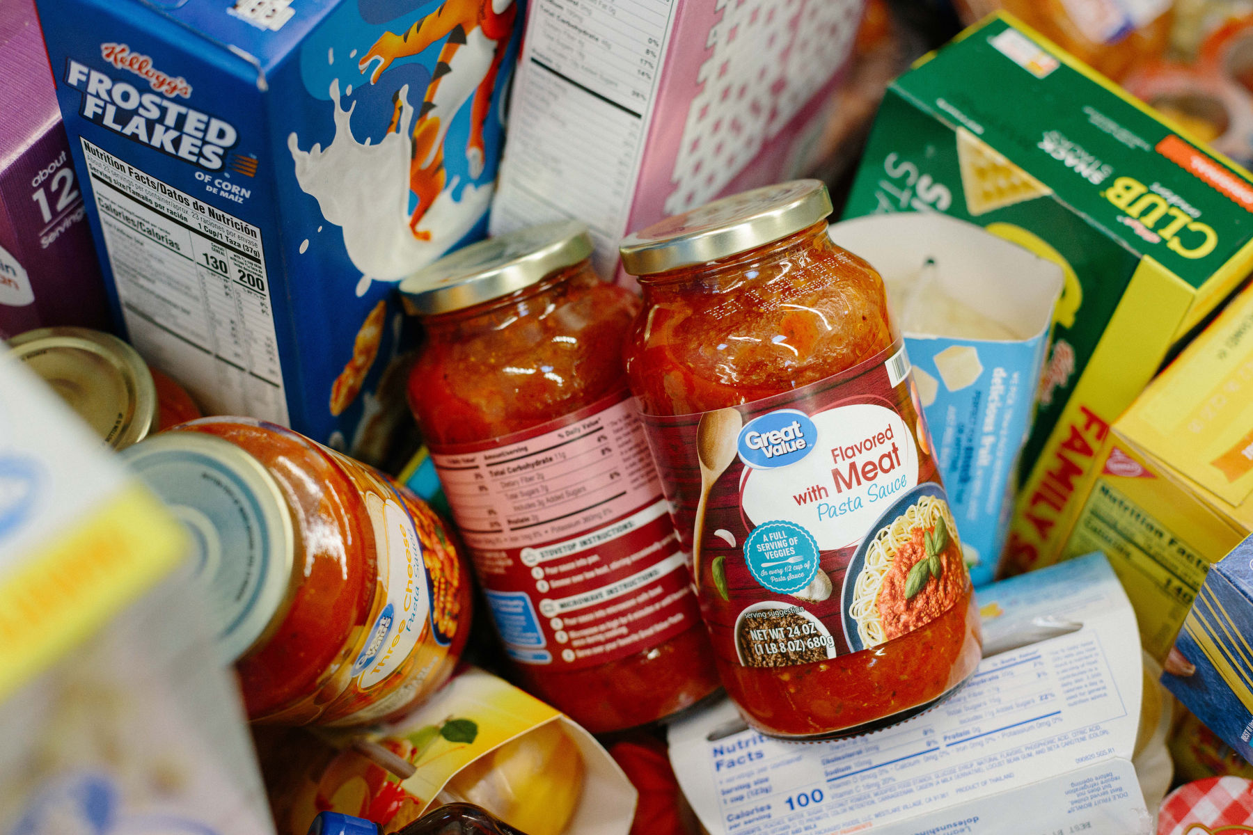 A closeup on items in a grocery cart, including spaghetti sauce, cereal and crackers.