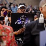 A crowd of Black women laugh and hold signs saying 