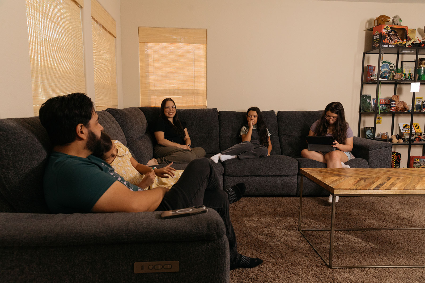 Jasmine Lopez sitting with her husband Jeremy and their three daughters on a gray sectional couch in their living room.