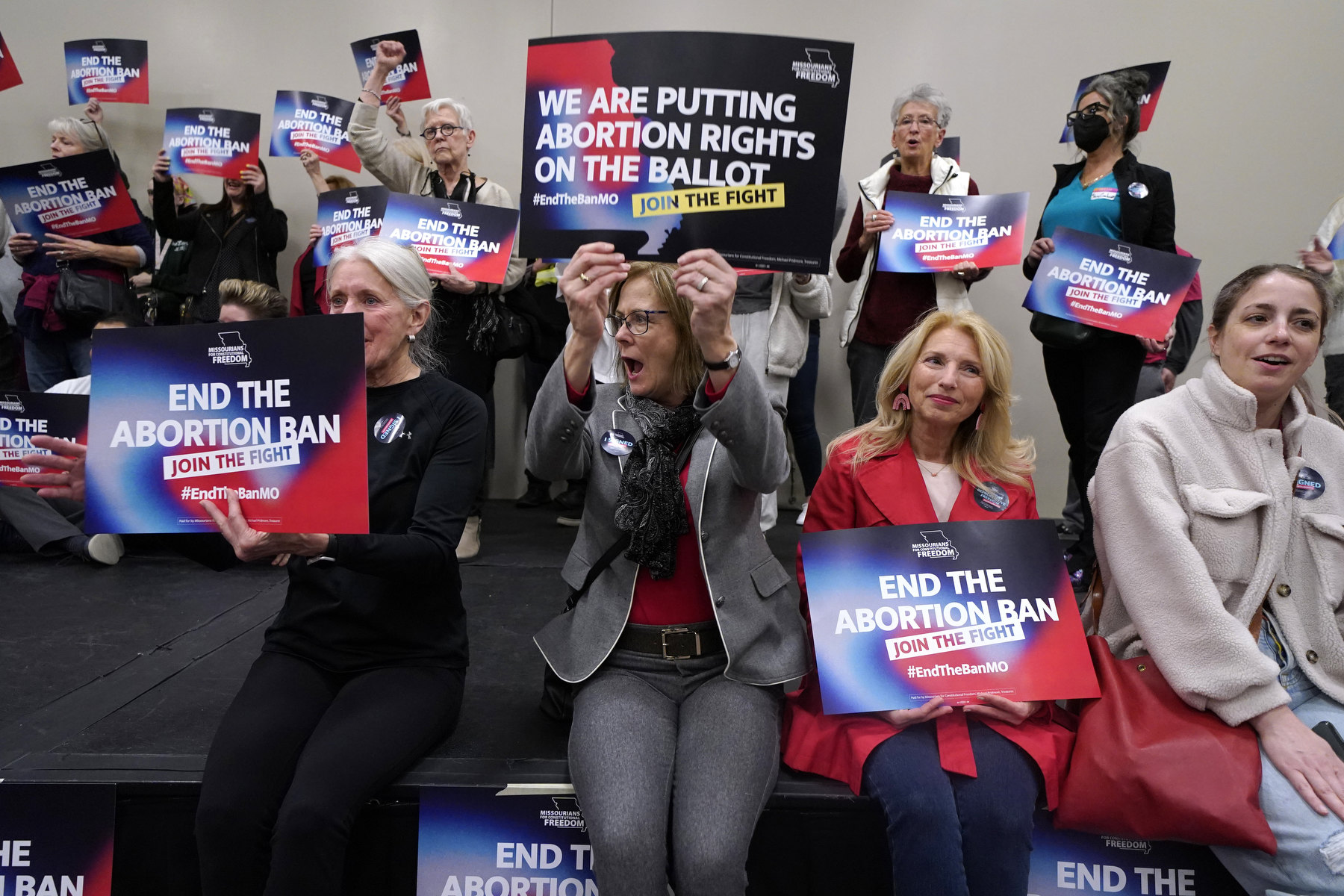 A group of women cheer as they hold signs saying "end the abortion ban".