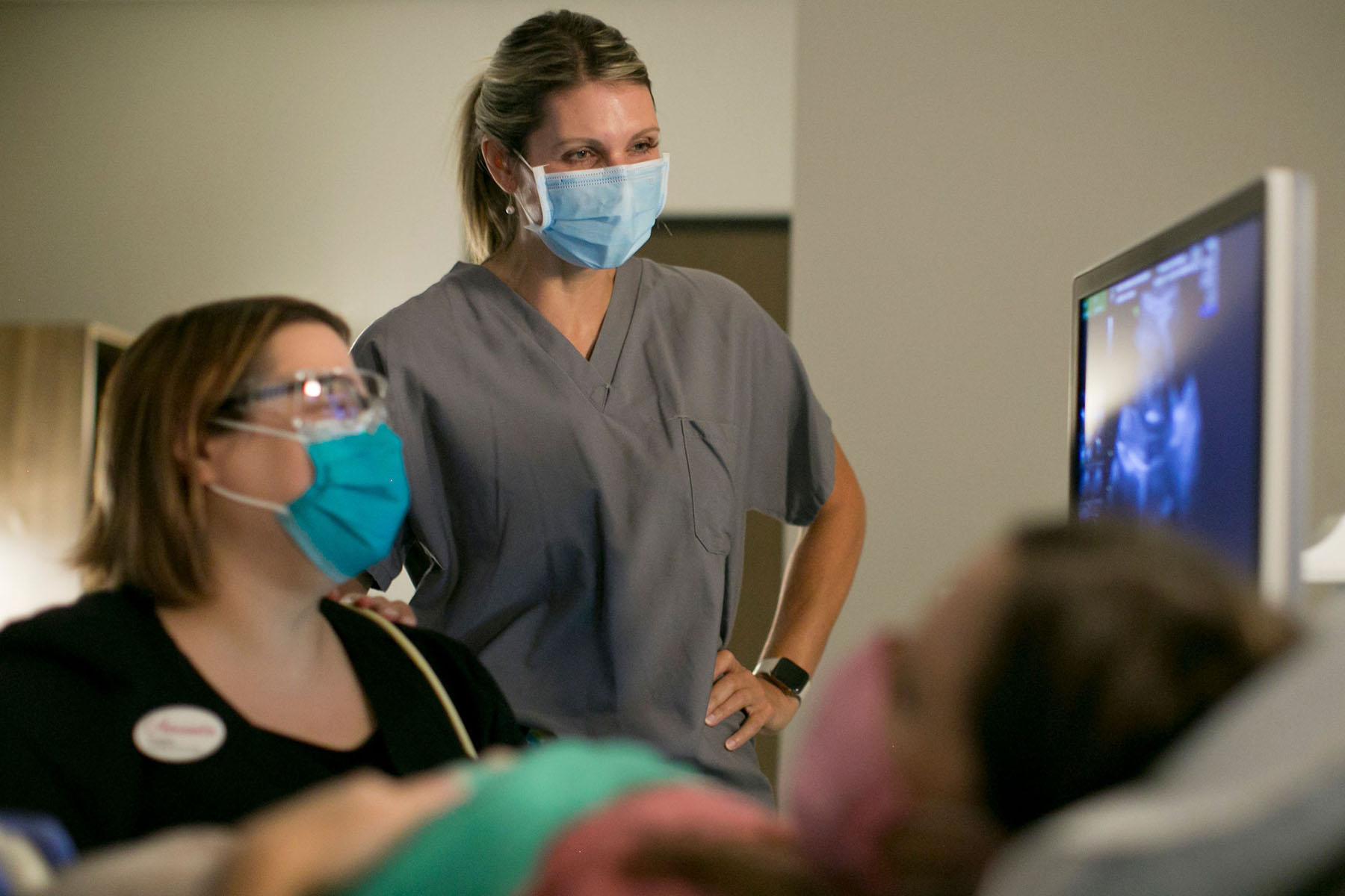 Dr. Kirstin Lyerly in medical scrubs stands beside another medical professional during a patient consultation, both wearing masks.