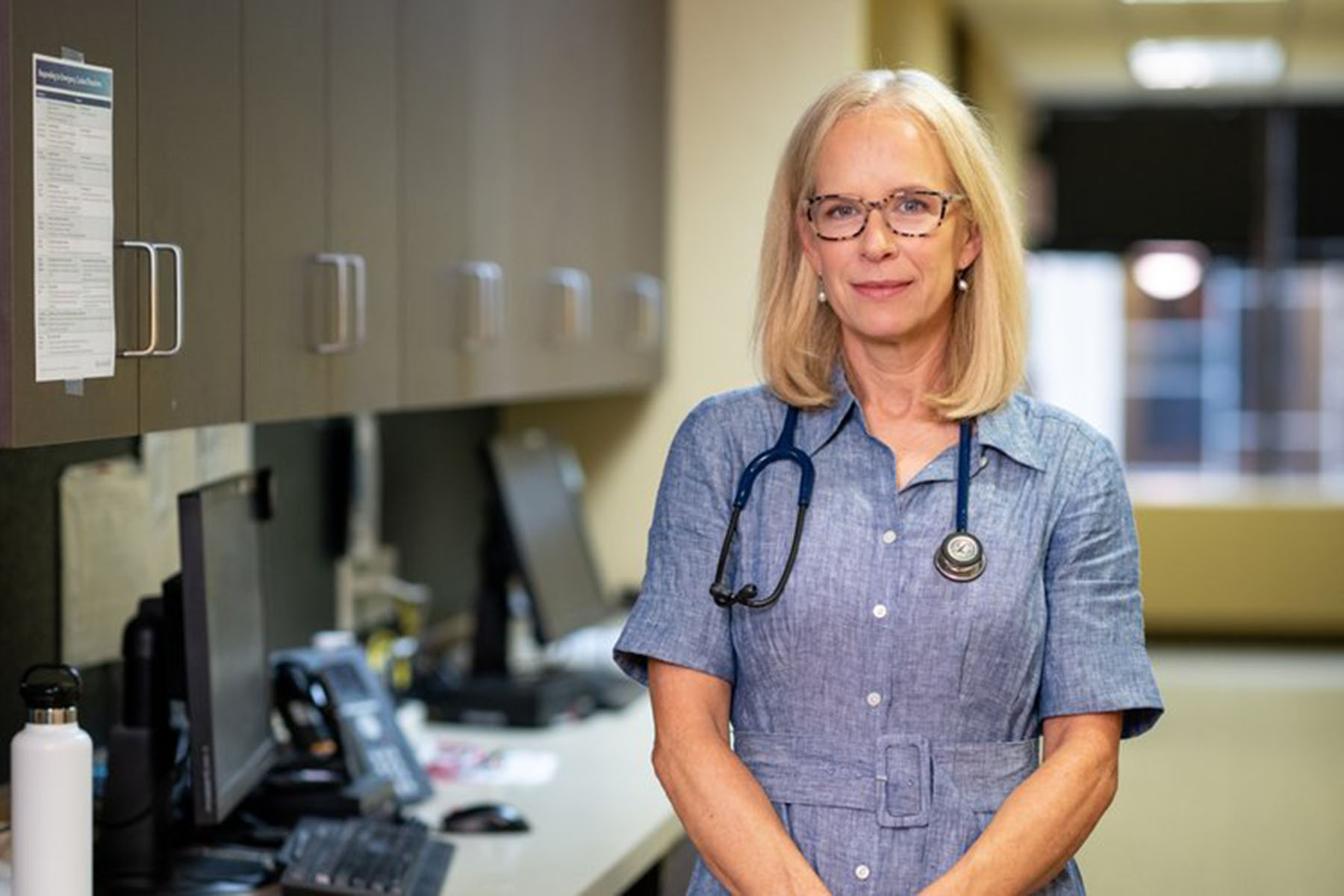 Dr. Kelly Morrison stands in a medical office wearing a stethoscope around her neck.