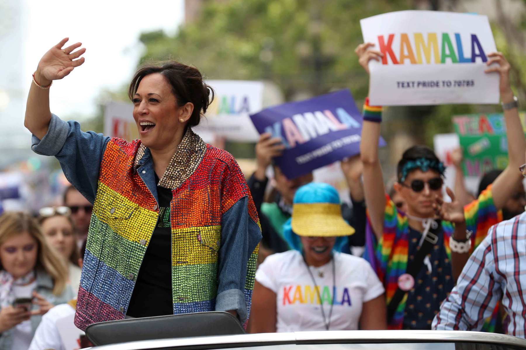 Kamala Harris waves to a crowd while in a car that is part of a Pride parade.