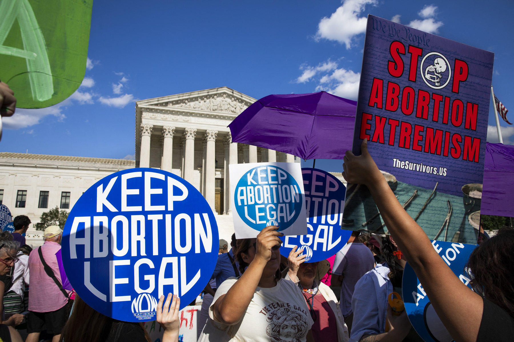 A crowd of people hold signs saying "keep abortion legal" and "stop abortion extremism" with the Supreme Court in the background.