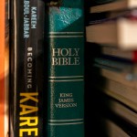 A Bible sits on a bookshelf among other books.