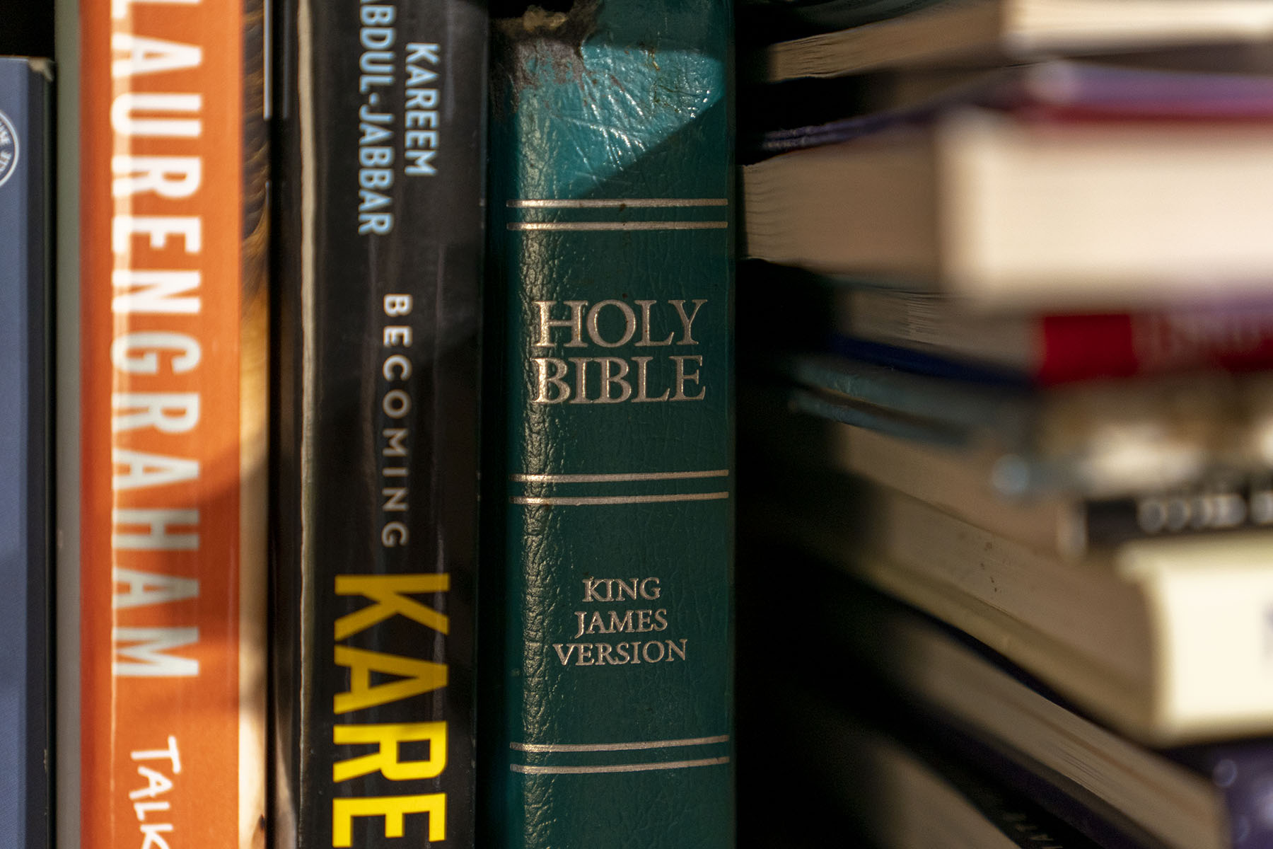 A Bible sits on a bookshelf among other books.