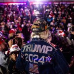 A crowd of people attend a Town Hall event with former President Trump, with a focus on a woman wearing a denim jacket with 