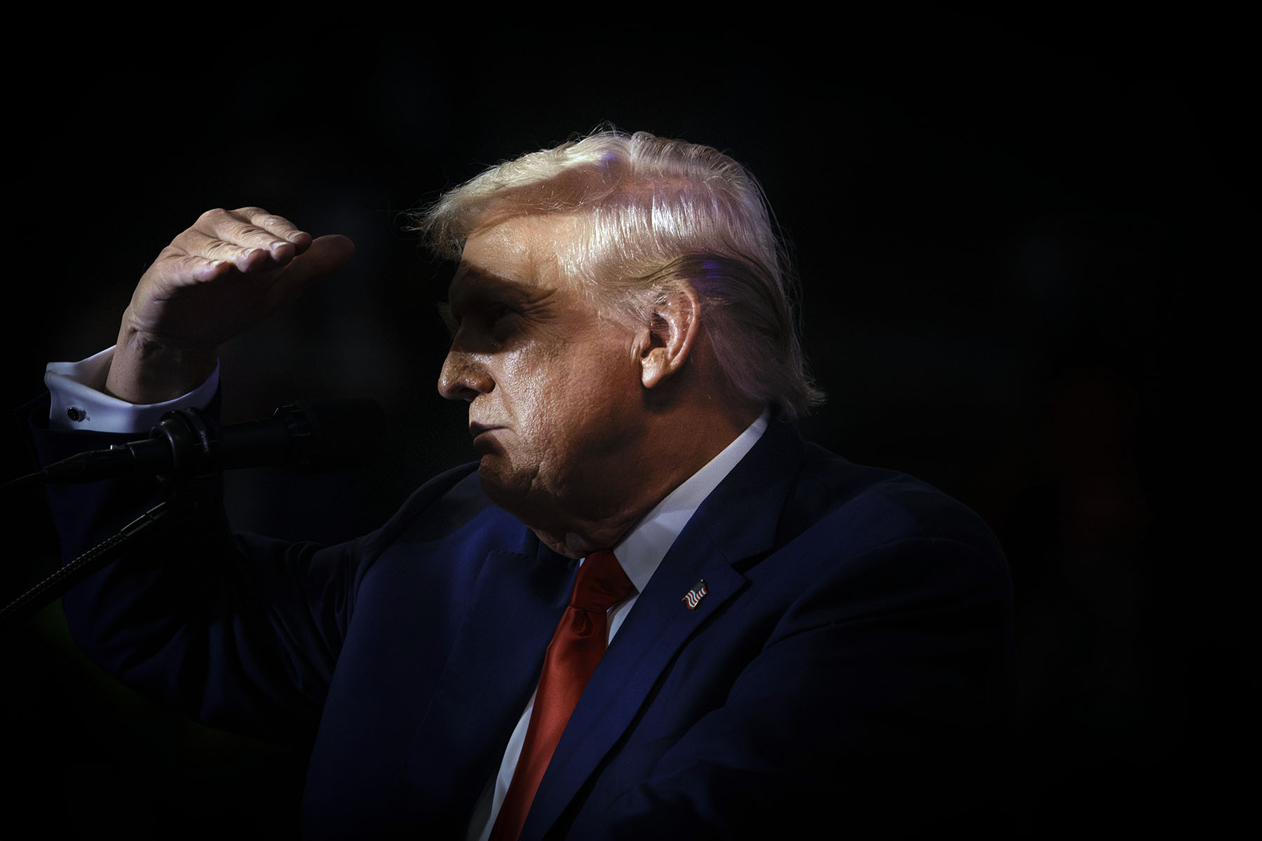 Donald Trump raises his hand to his forehead to block out light while looking into the distance.