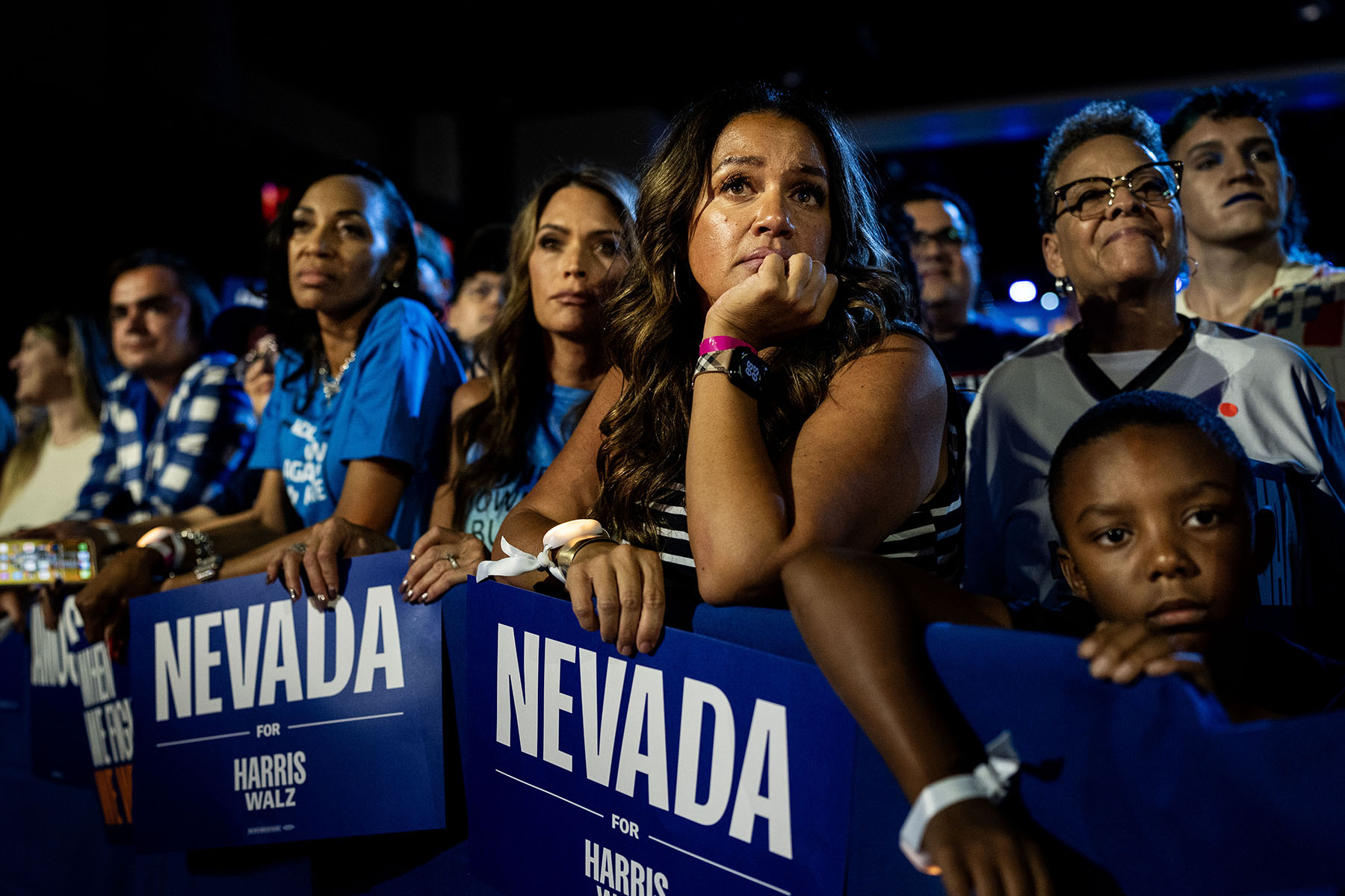 A group of Nevada voters at a rally in Las Vegas, holding blue signs that read "Nevada for Harris Walz," while listening to Kamala Harris speak on stage.