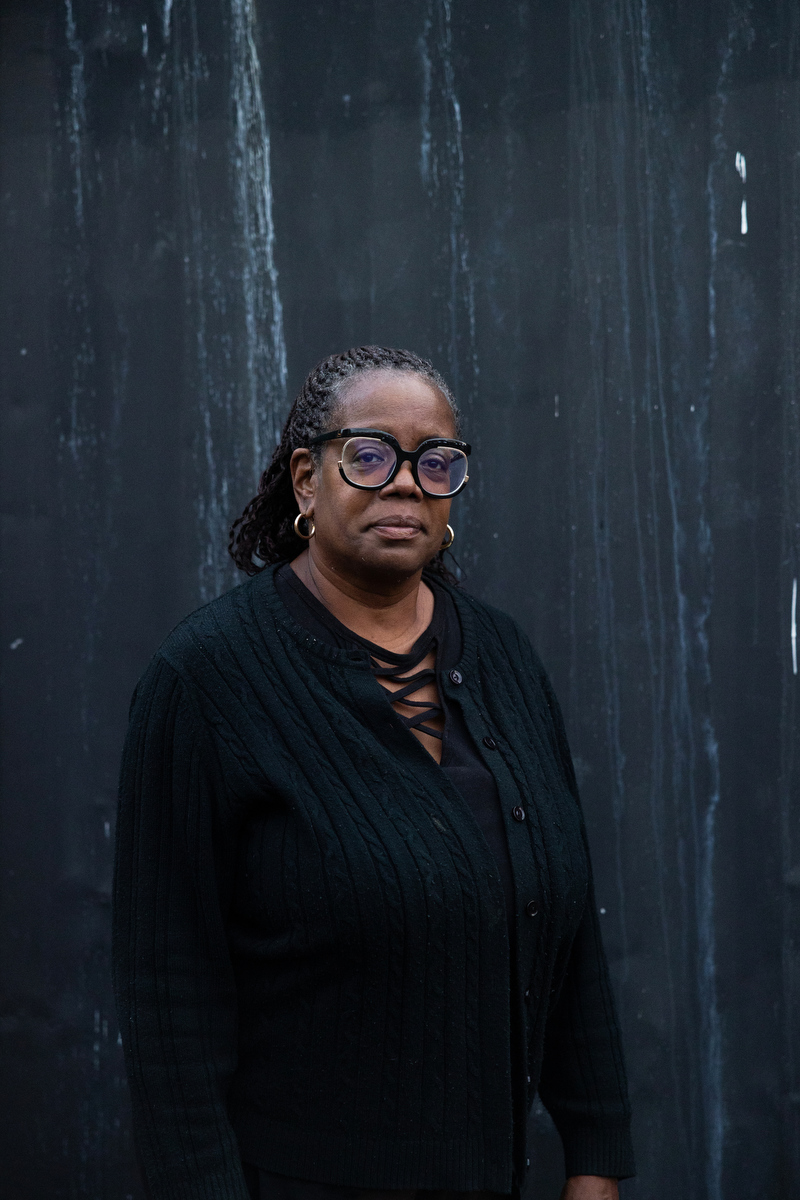 A woman wearing all black stands against a black background.