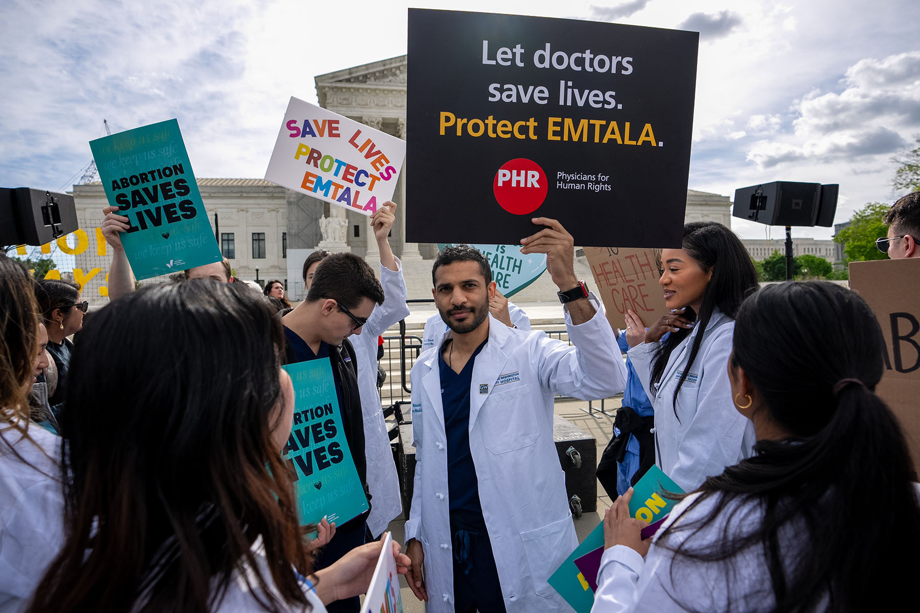 A group of doctors joins abortion rights supporters at a rally outside the Supreme Court. One holds a sign that reads "Let doctors save lives. Protect EMTALA."