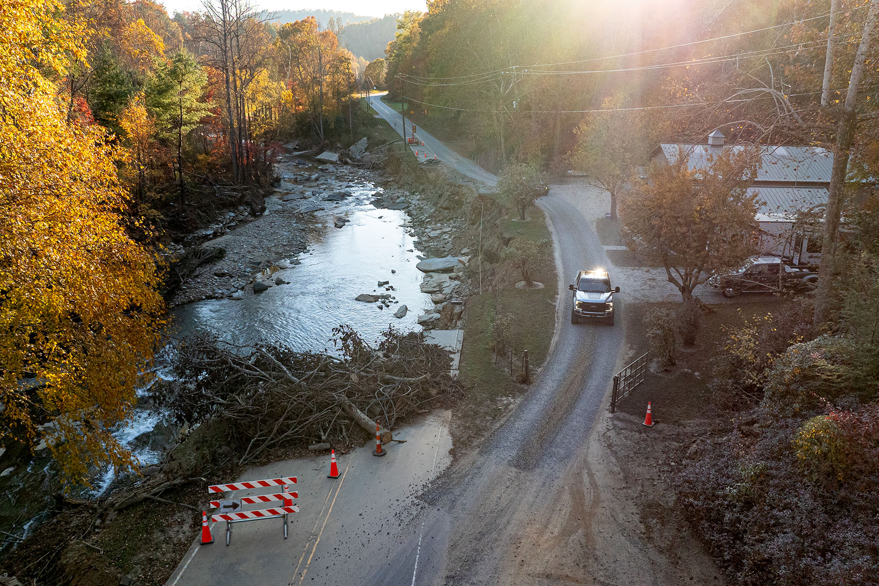 An overhead view of a rural county road where part of the road is obstructed by a tree and ends in a creek.