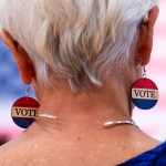 A woman, seen from the back, wears earrings that read 