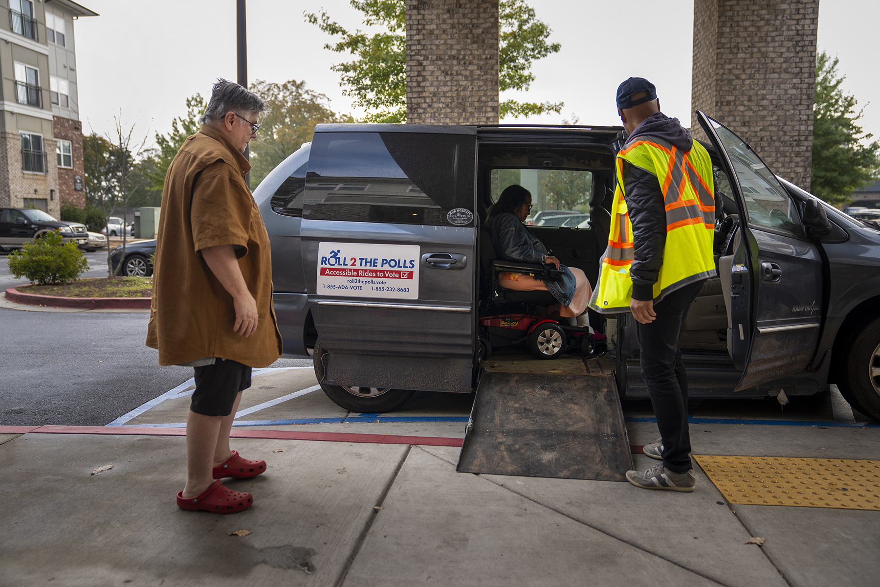 Elisabeth Huhn (left) and Roll 2 the Polls volunteer Sam Soremekum (right) assist Cathy Johnston, 70, into a Roll 2 the Polls van.