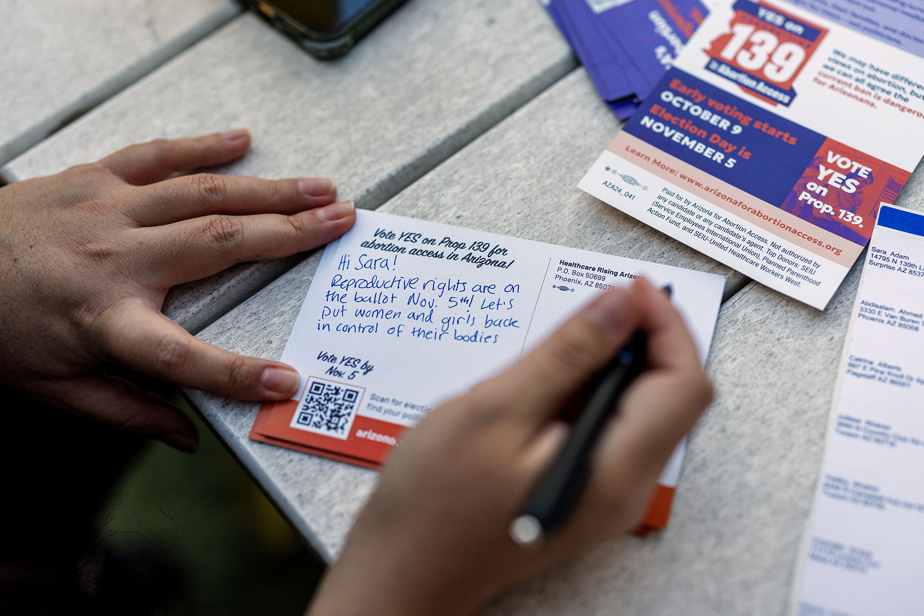 An abortion activist fills out a postcard to send out to a voter for in Phoenix, Arizona. The postcard reads "Hi Sara! Reproductive rights are on the ballot Nov. 5th! Let's put women and girls back in control of their bodies."