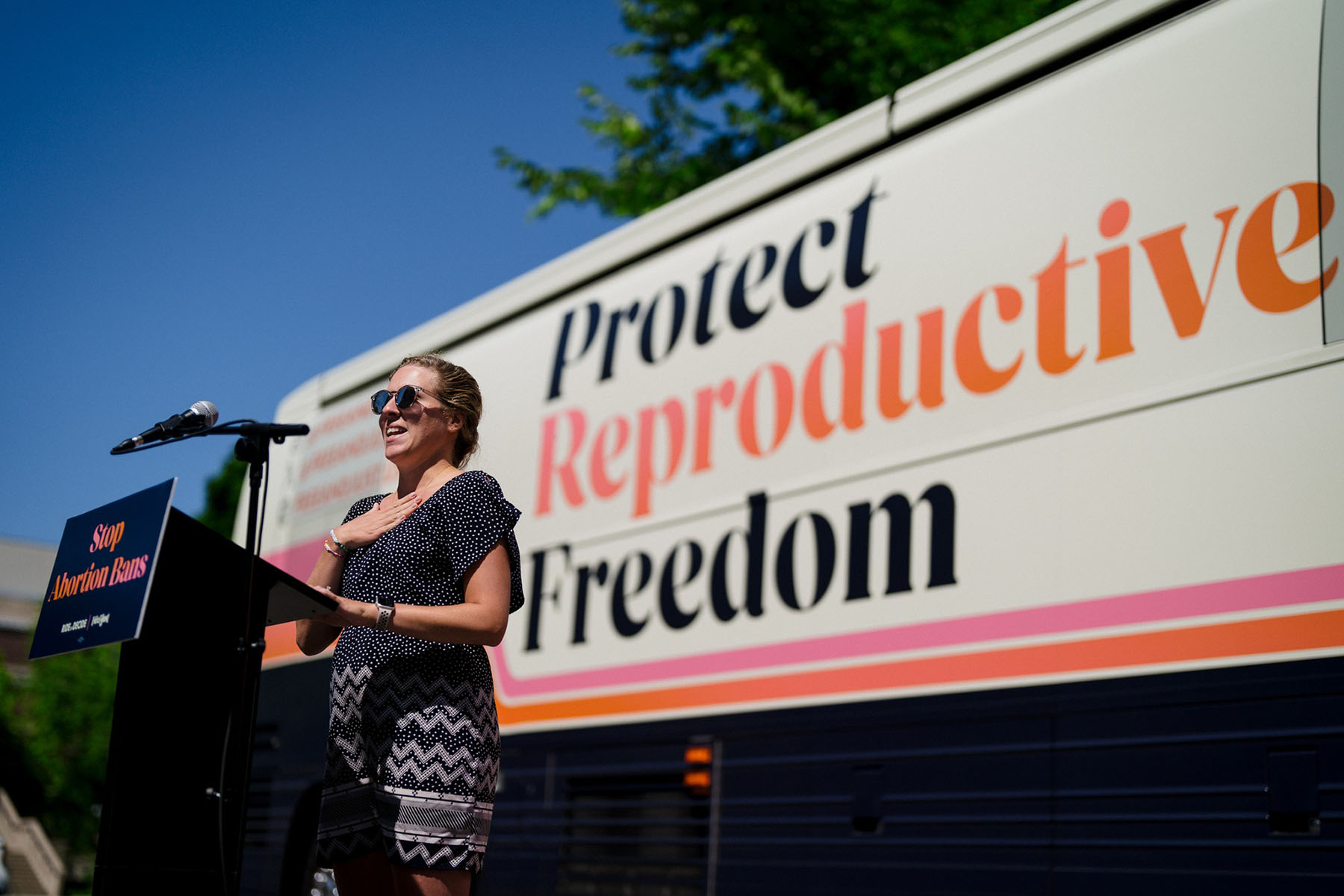 Gracie Ladd speaks in front of a bus on which is pained "Protect Reproductive Freedom."