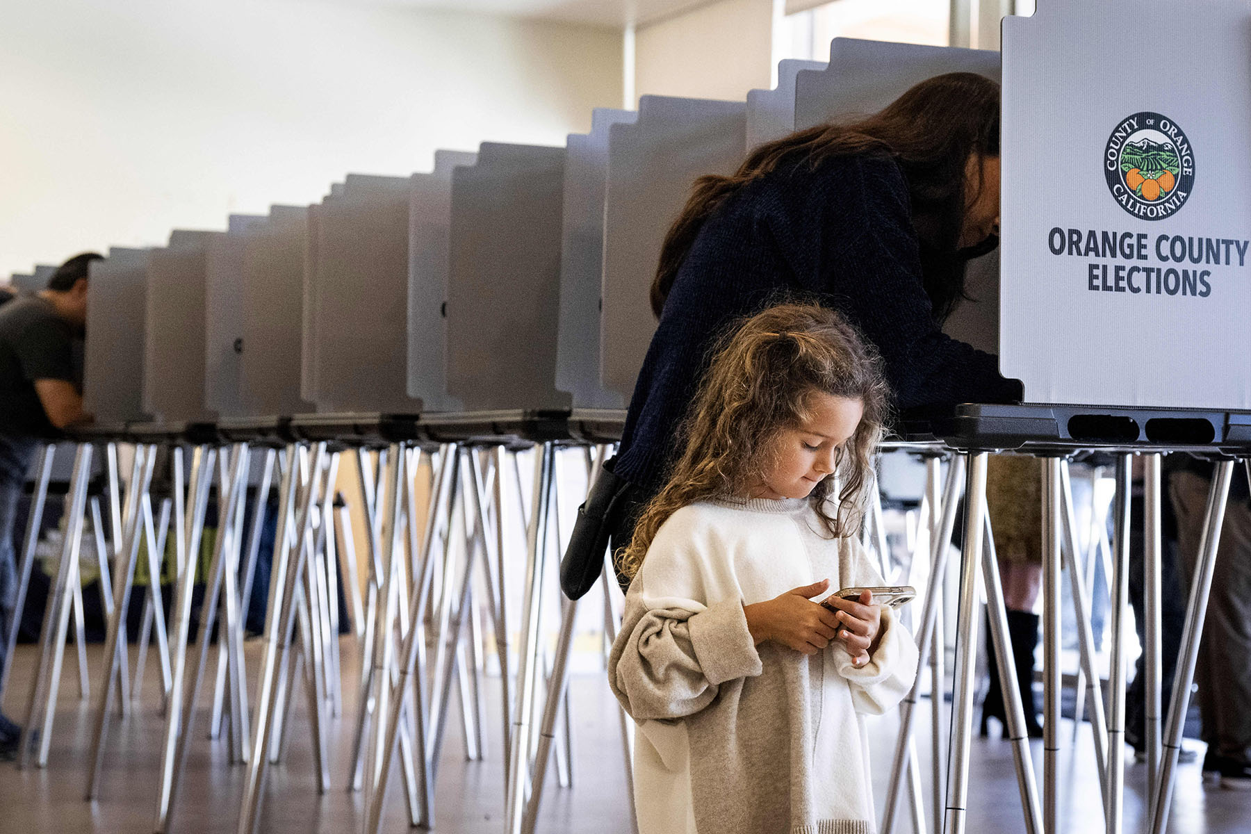 A little girl plays on a phone as her mom votes behind her at a polling place in Lake Forest, California.