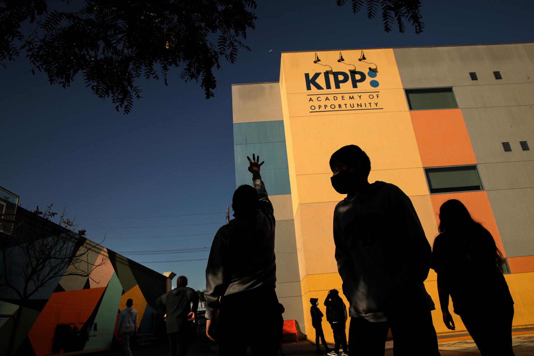 Children play outside of a charter school, in the shadow of a brightly-colored building.