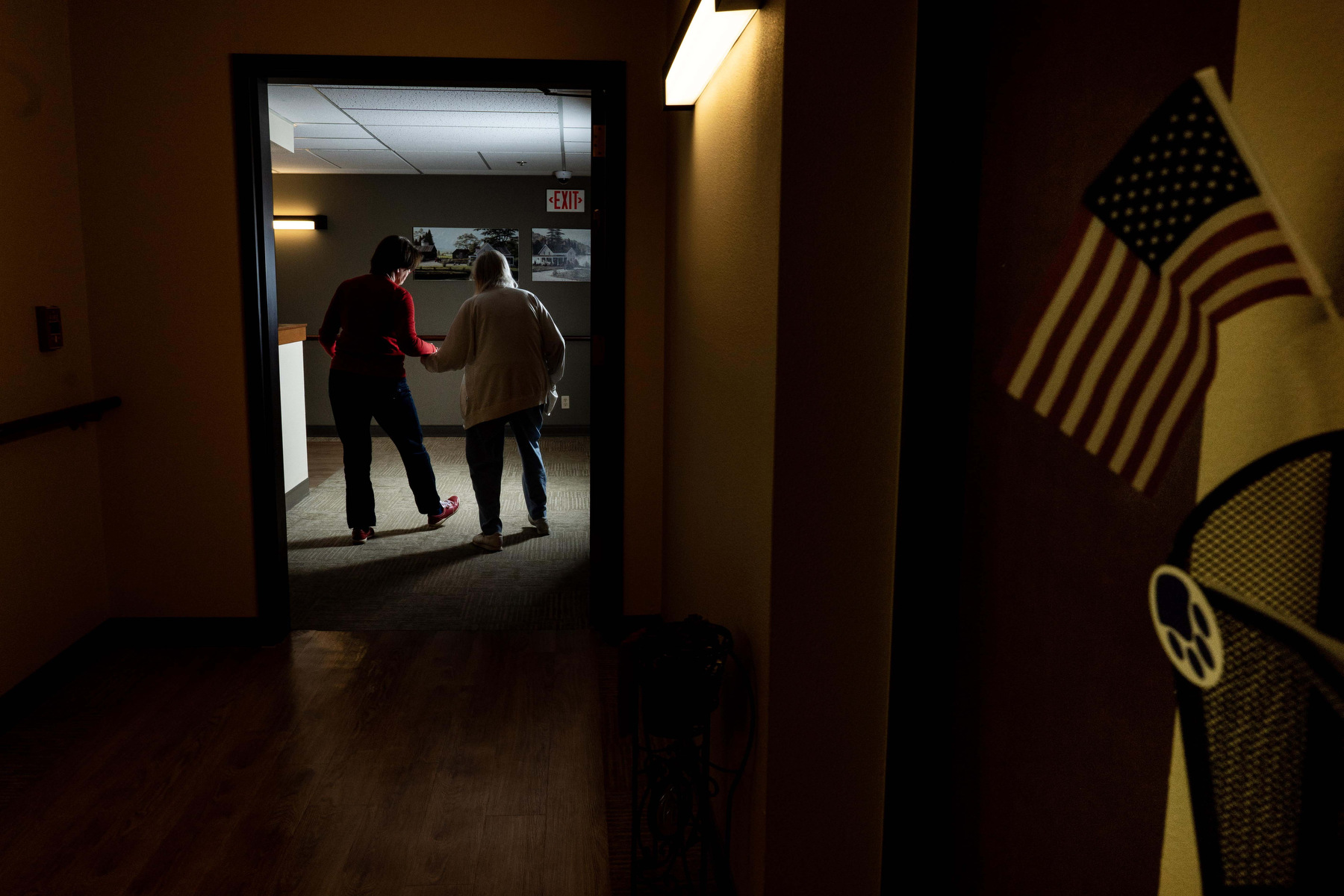 Two women dance down a hallways, framed by a door with an American flag in the foreground.