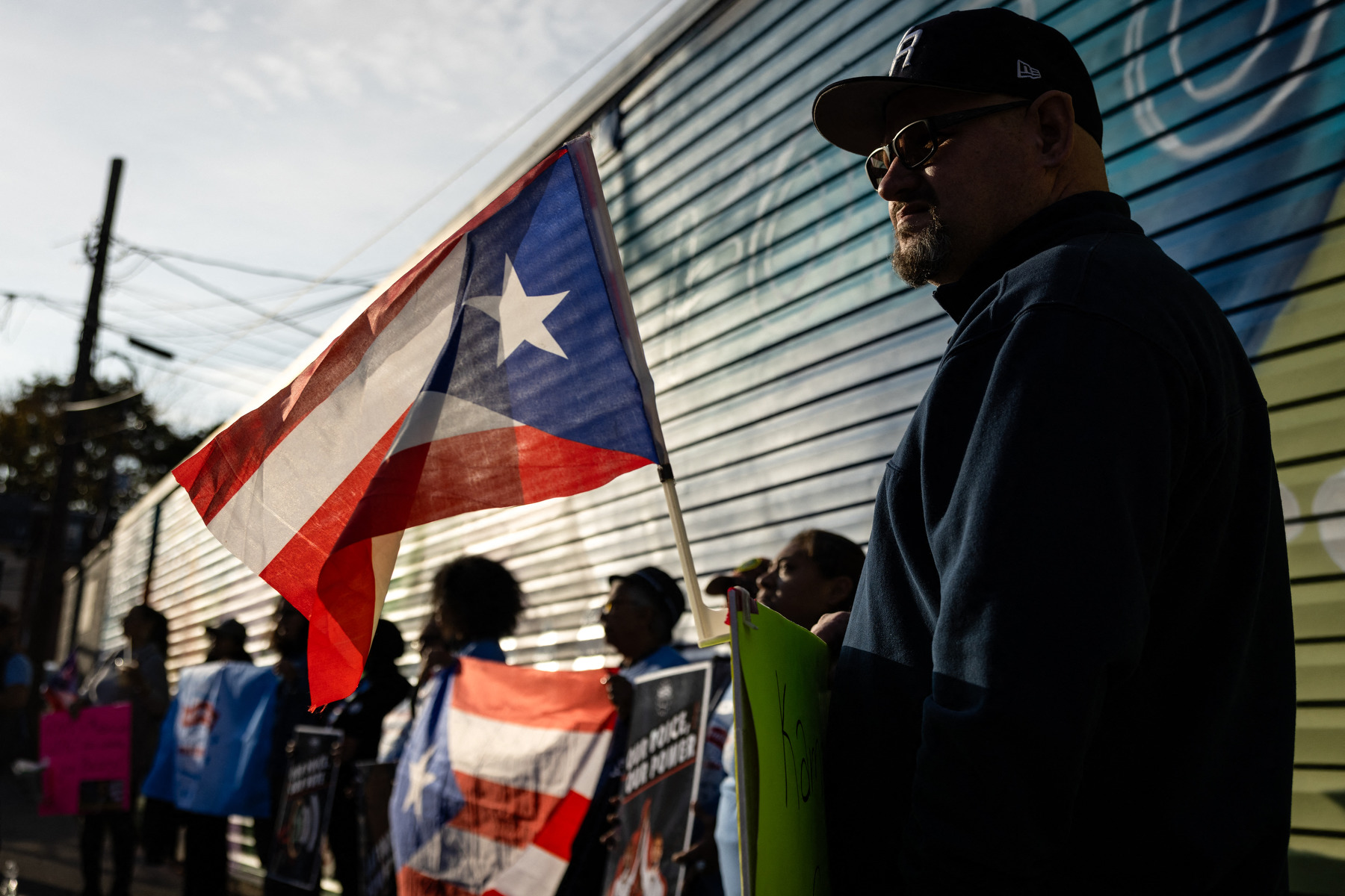 A man holds a Puerto Rican flag alongside a line of several other people also holding flags and signs.