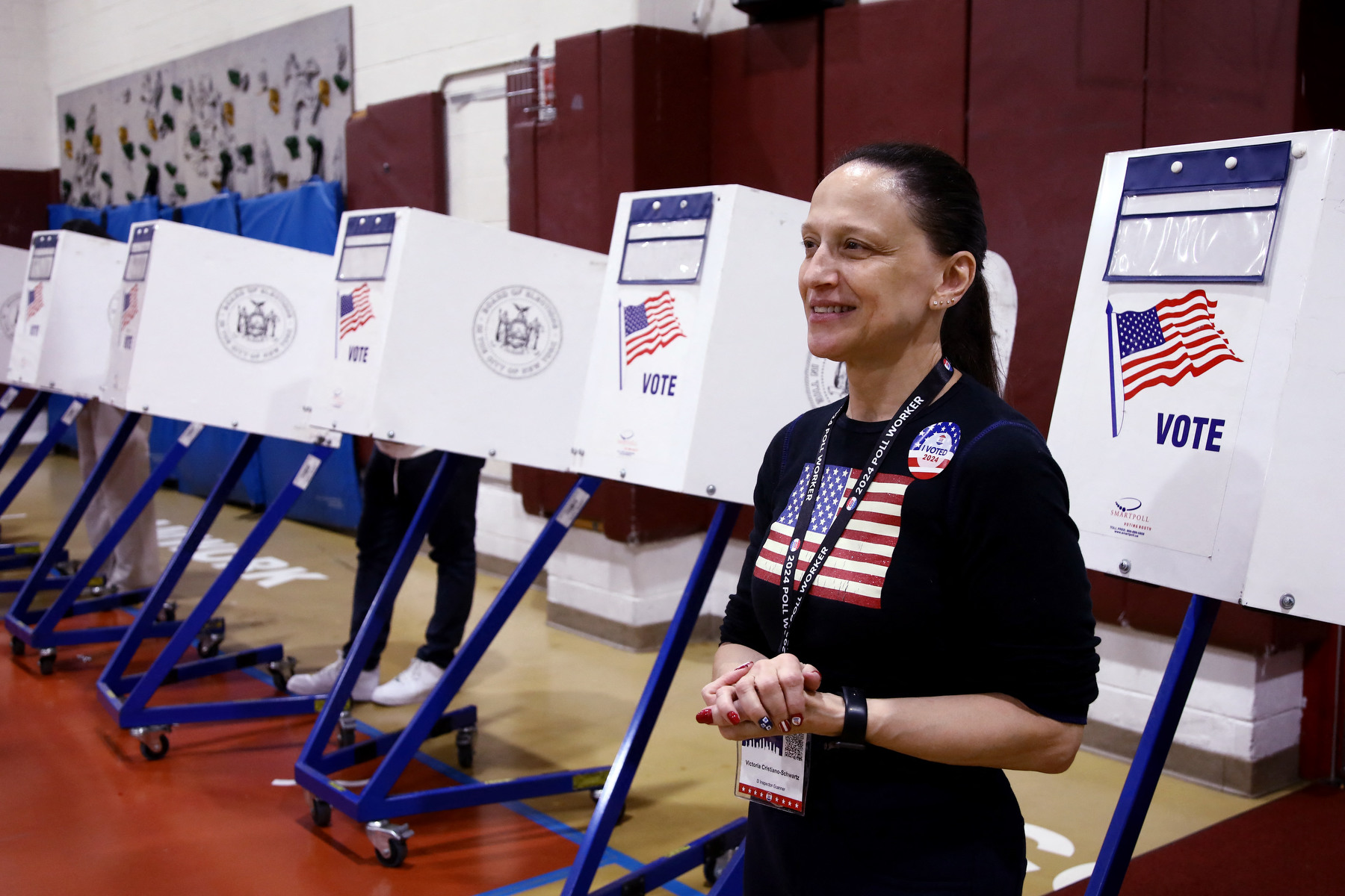 A woman stands in front of a line of voting booths.