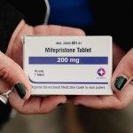 A closeup on hands with chipped nail polish holding a box that says mifepristone.