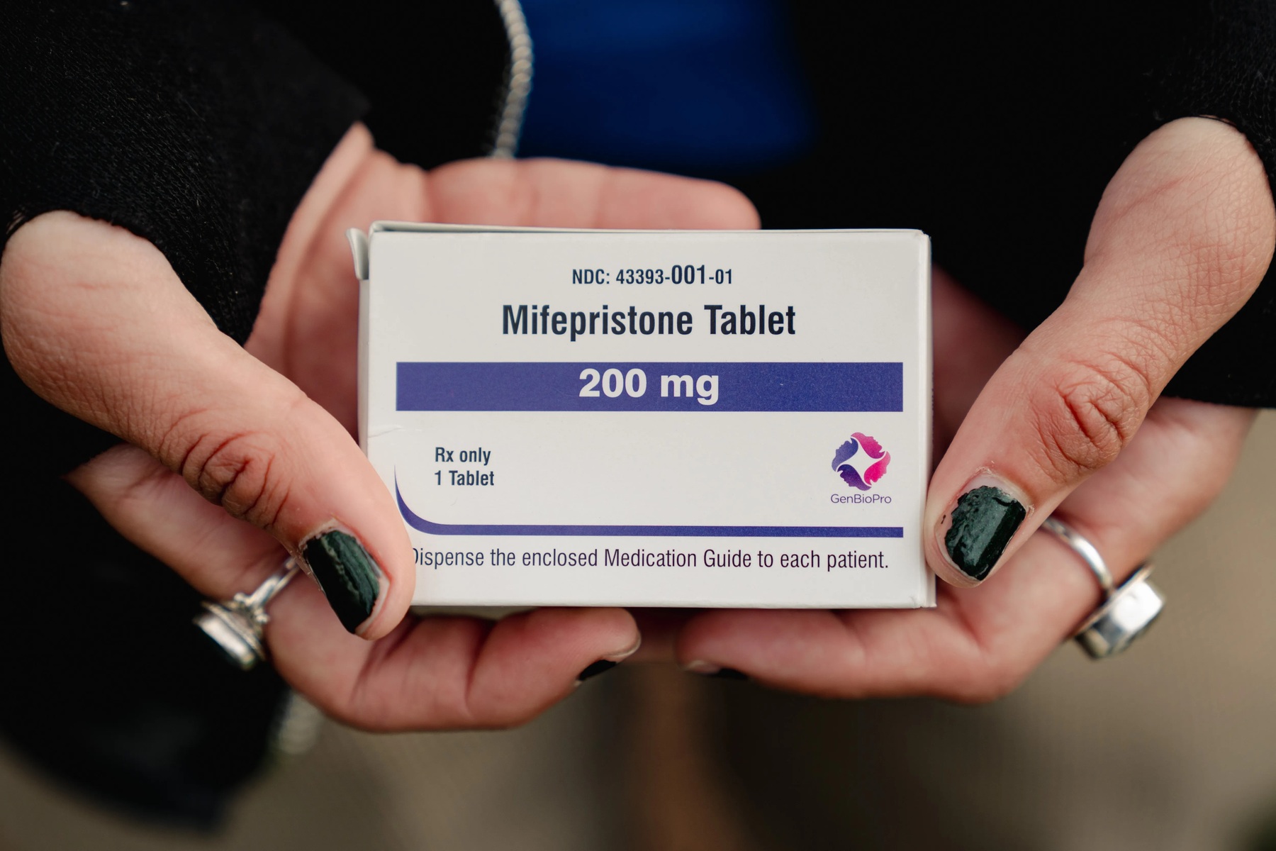 A closeup on hands with chipped nail polish holding a box that says mifepristone.